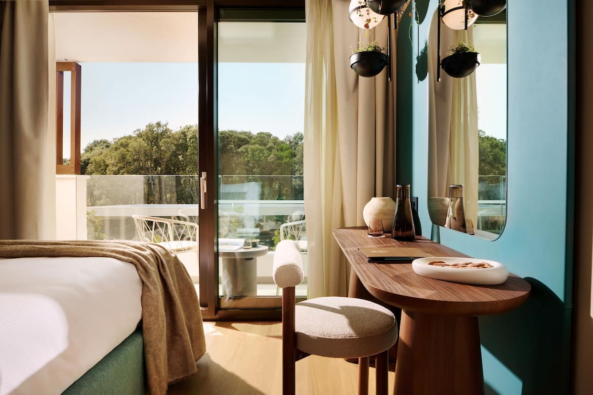 A modern bedroom with a large bed, a wooden desk, and a view of the outdoors.