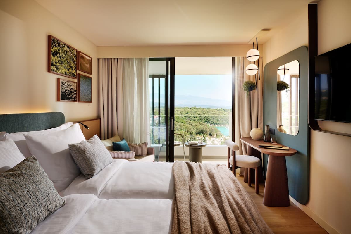 A hotel room with a large bed, a desk, a chair, and a view of the outdoors.