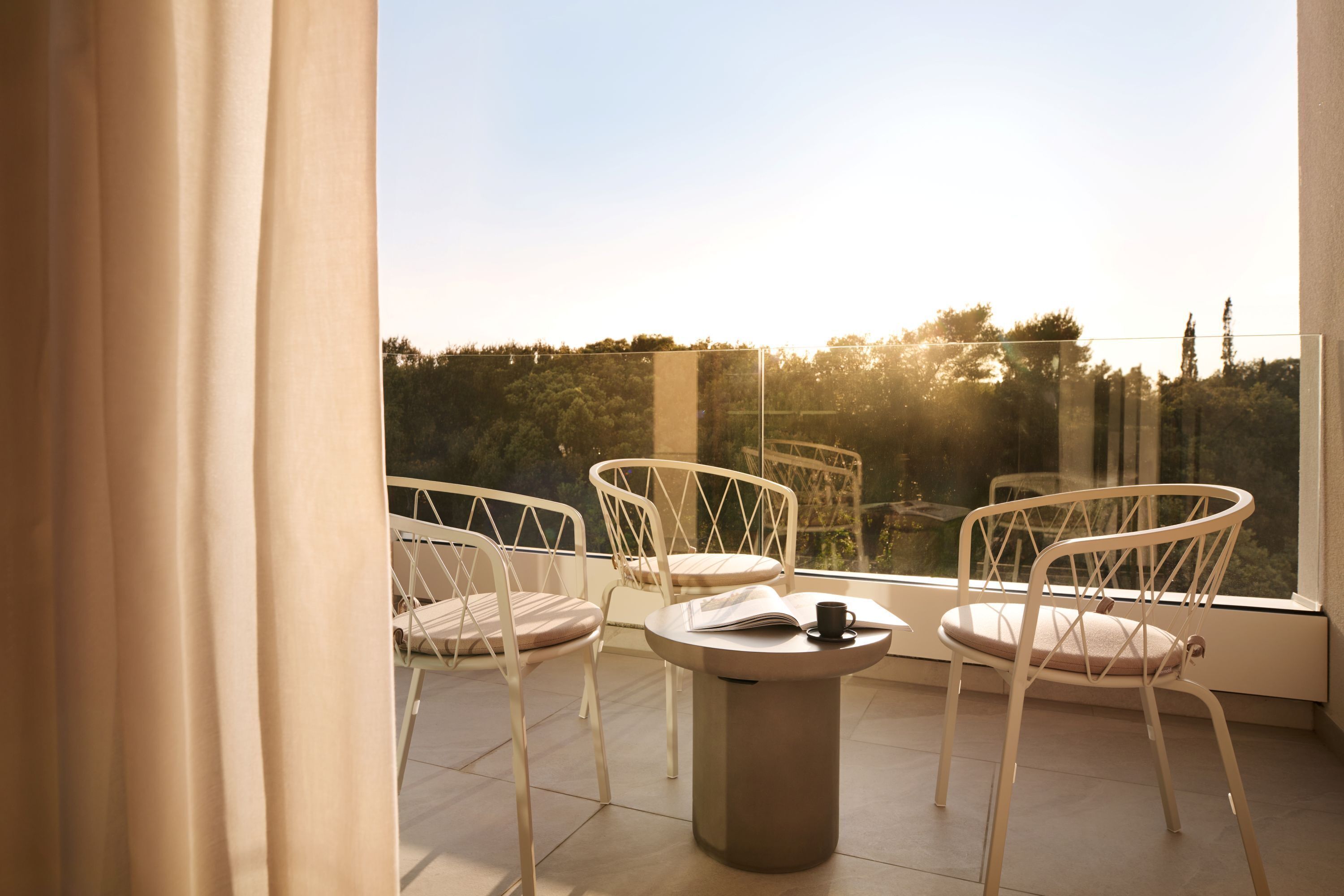 Een balkon met twee witte stoelen en een kleine tafel, met uitzicht op een bebost gebied.