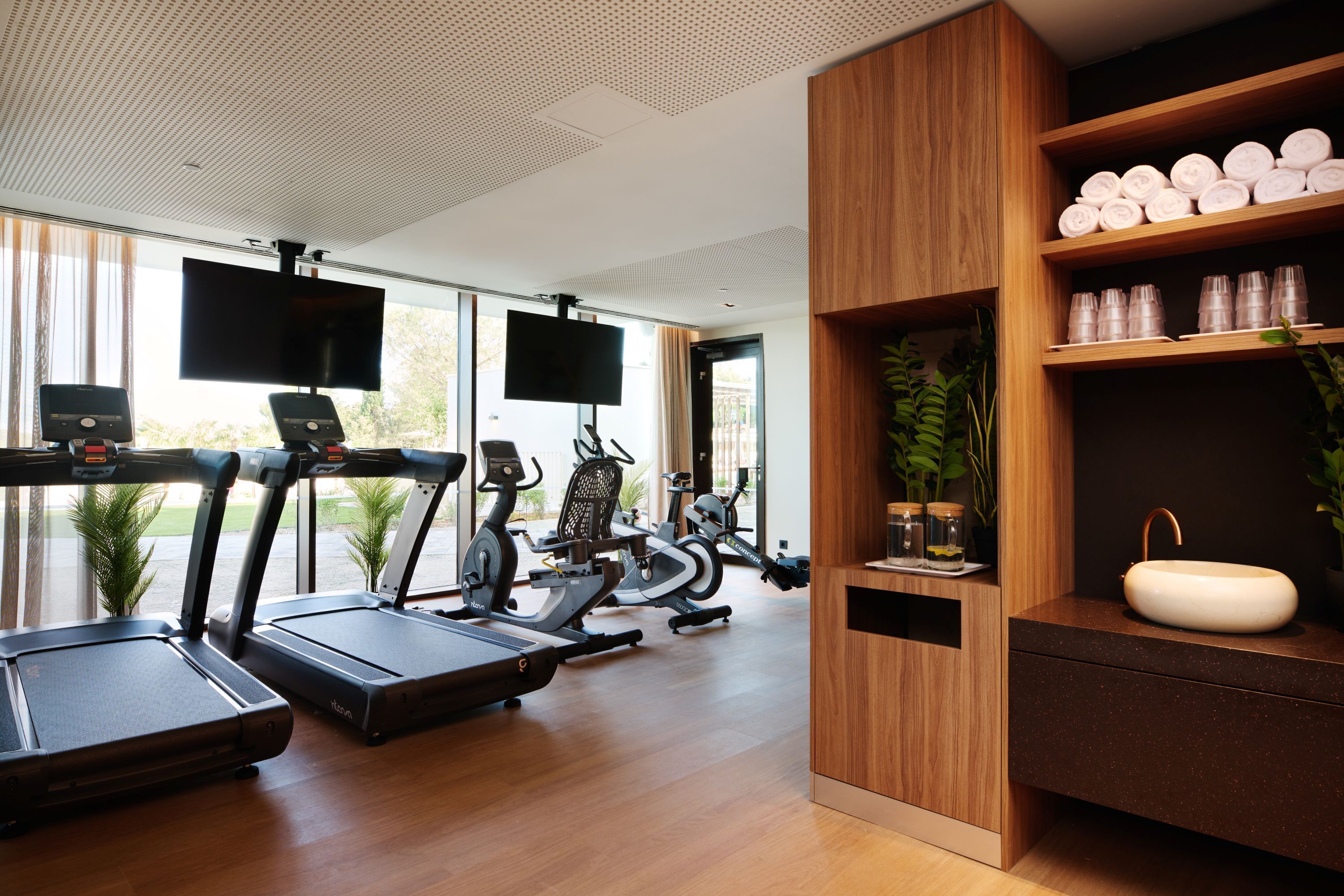 A modern gym with treadmills, stationary bikes, and a large TV screen.