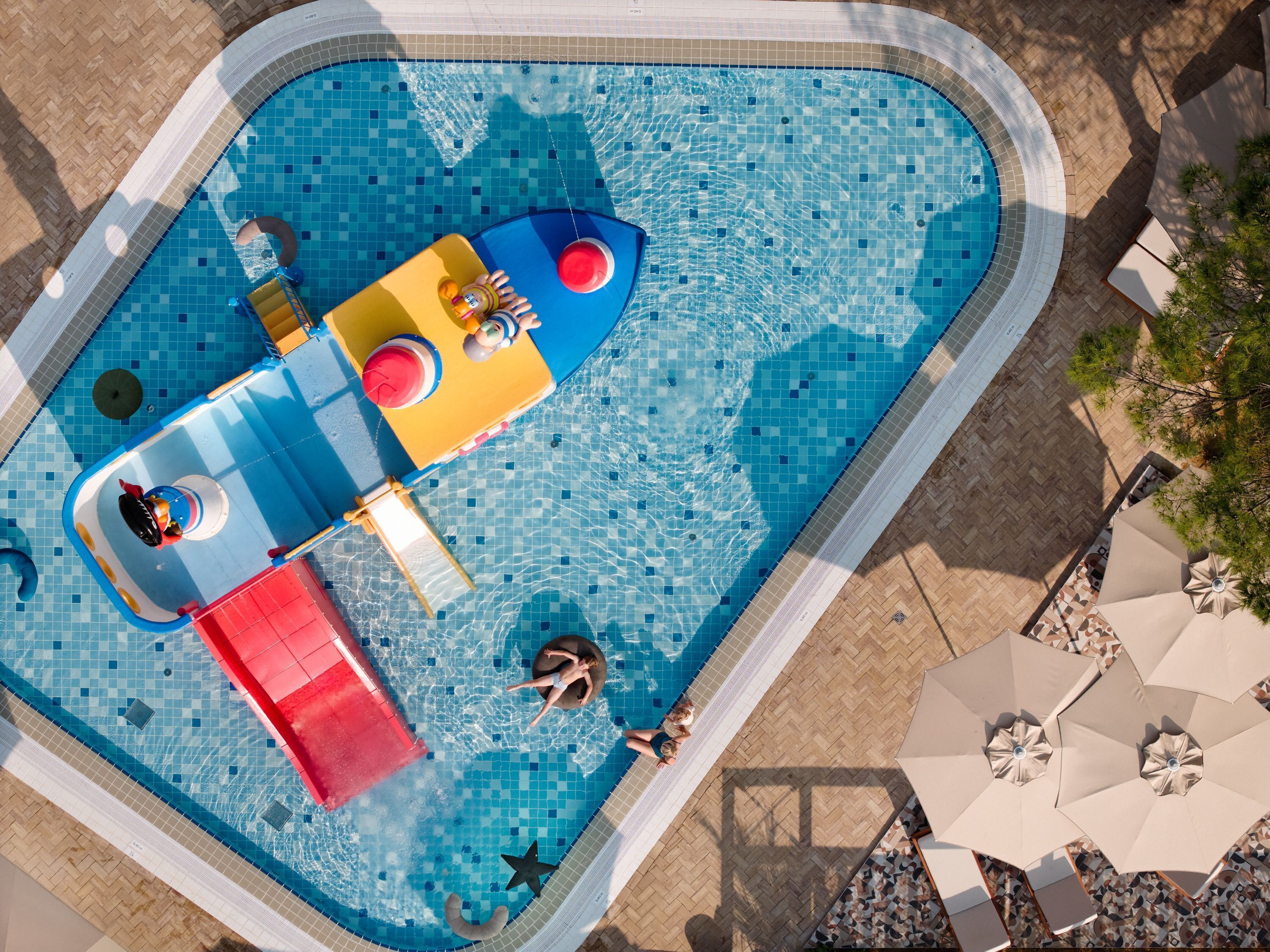 Vista aerea di una piscina con uno scivolo, una piccola barca e un lettino.