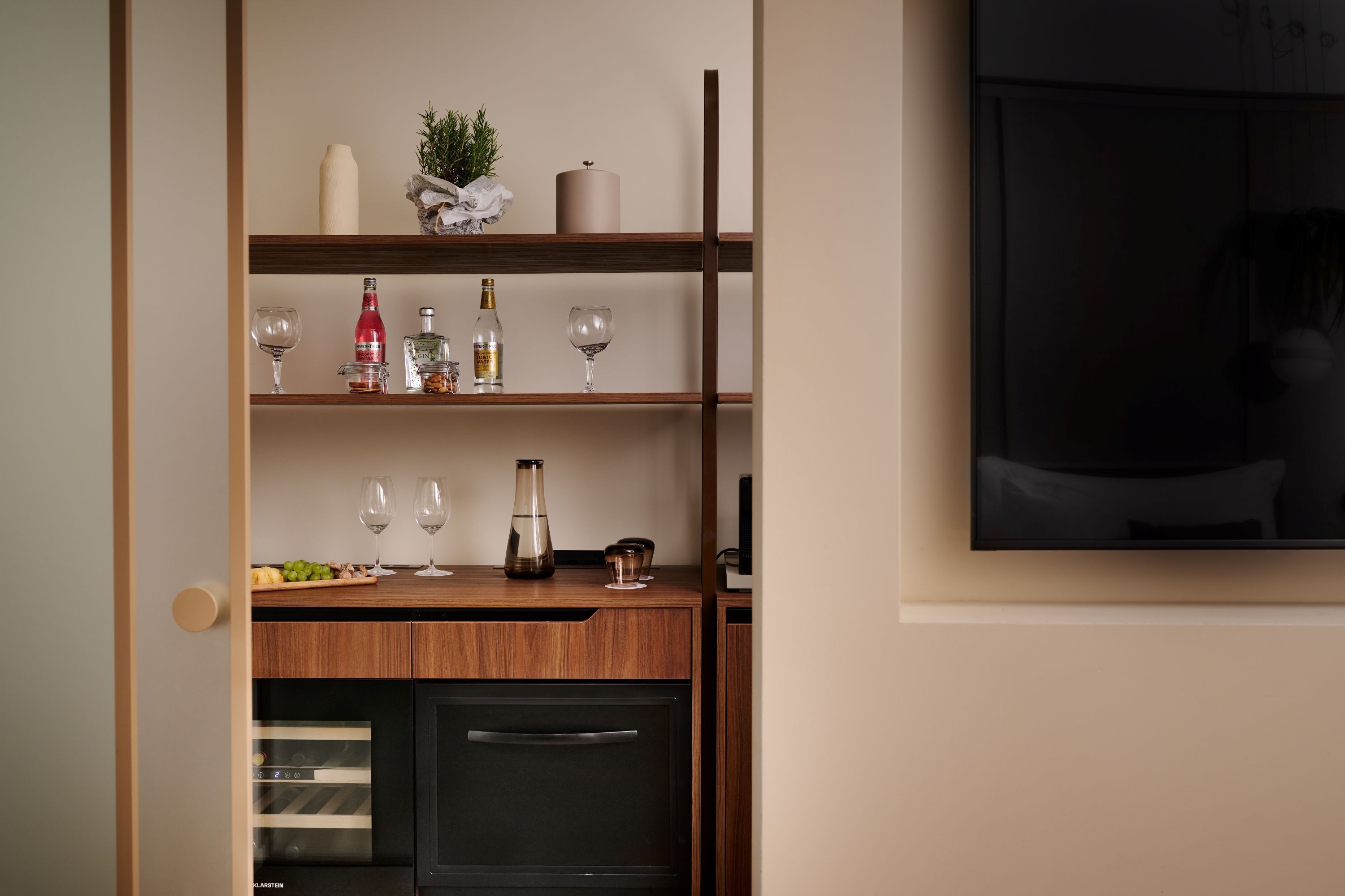 A kitchen with wooden shelves, wine glasses, bottles, and a TV.