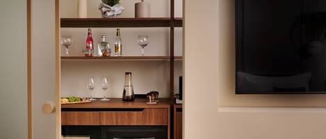 A kitchen with wooden shelves, wine glasses, bottles, and a TV.