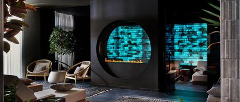 A modern living room with a circular fireplace, comfortable seating, and a large plant.