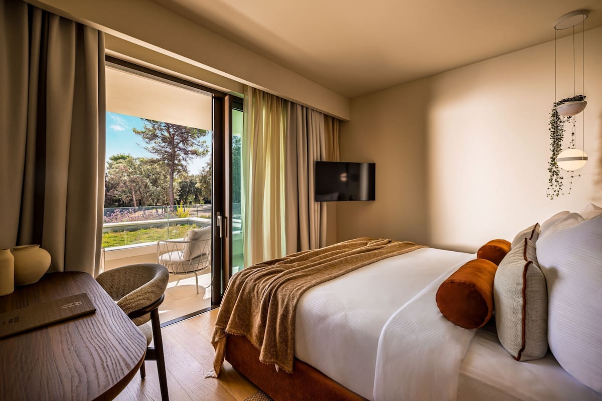 A hotel room with a bed, a TV, a table, and a view of the outdoors.