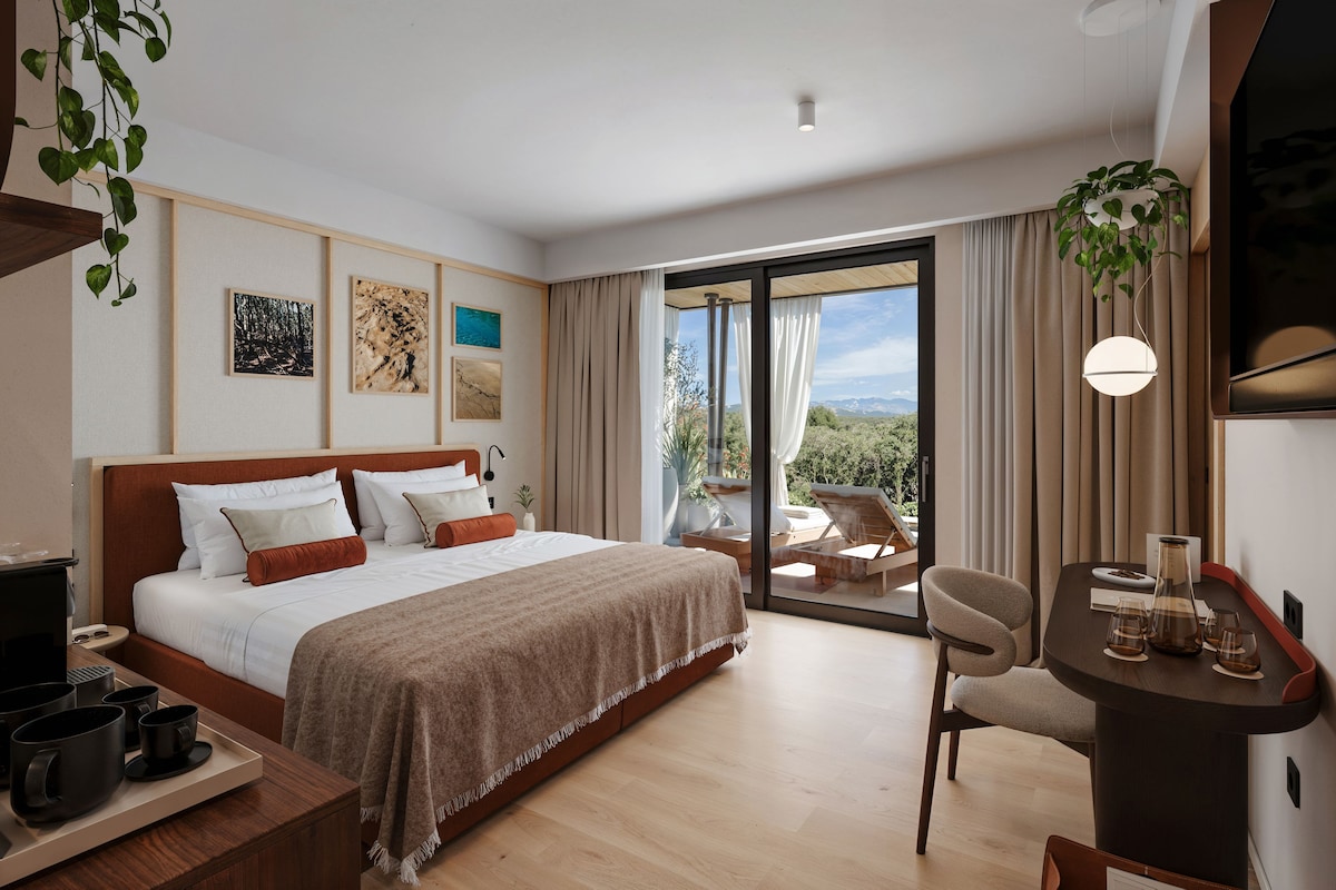 A hotel room with a bed, a desk, a chair, and a balcony with a view.