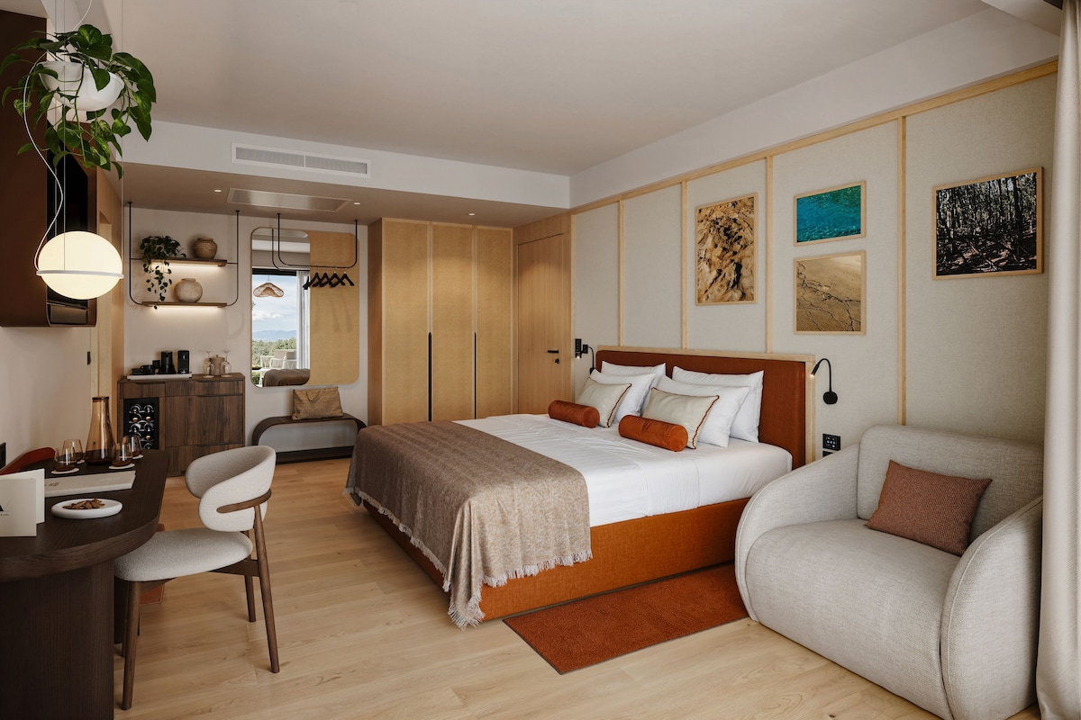 A modern hotel room with a large bed, a desk, a chair, and a sofa.