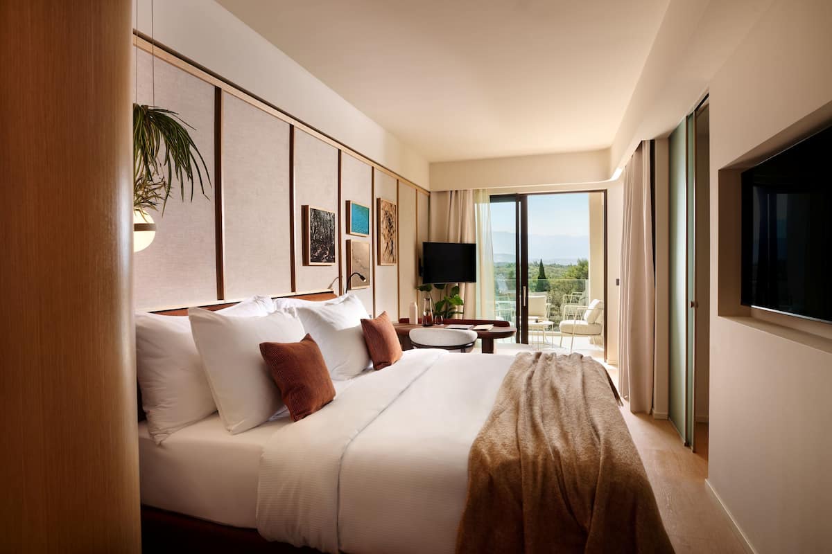 A hotel room with a large bed, a flat-screen TV, a small table, and a view of the outdoors.