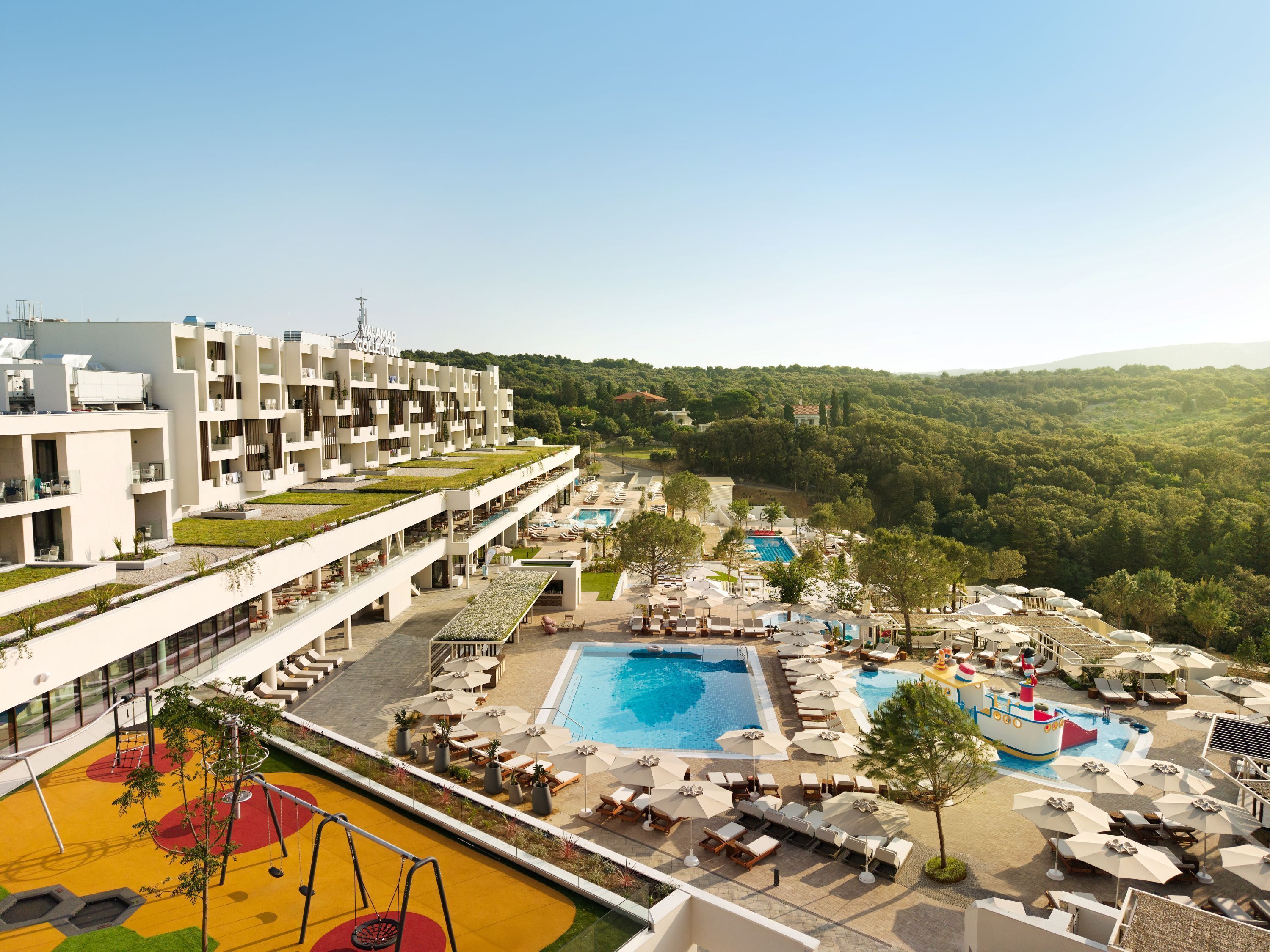 Un hotel con diverse piscine, un'area giochi per bambini e vista sulla foresta circostante.
