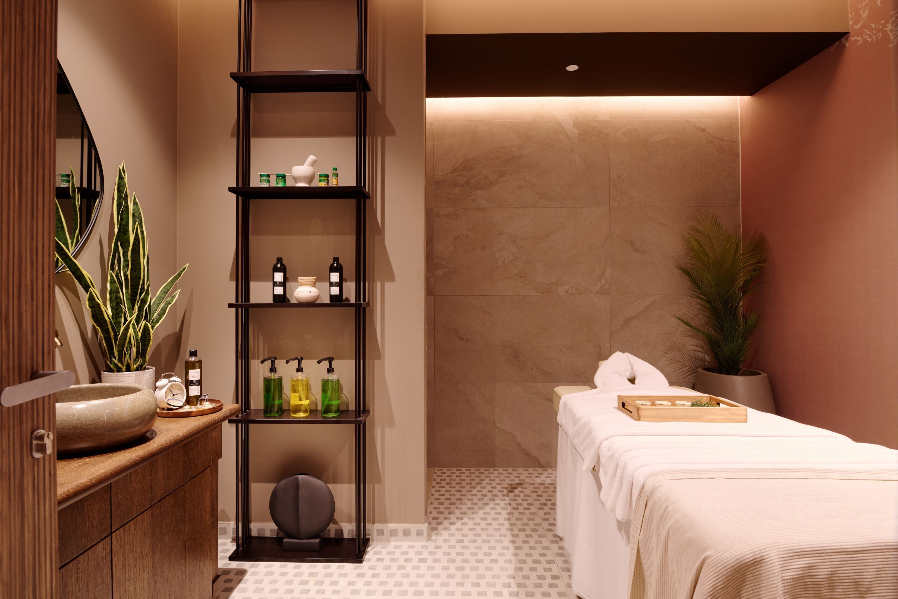 A modern bathroom with a wooden vanity, a shelf with toiletries, a towel rack, and a massage table.