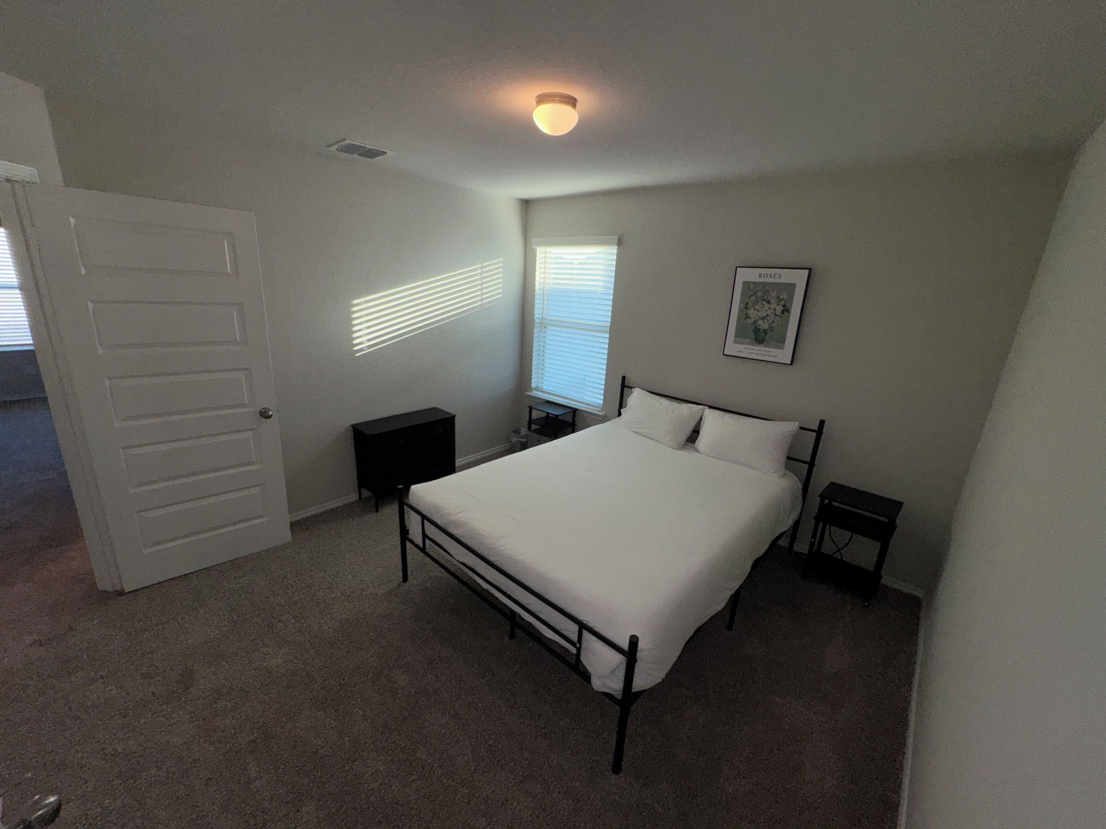 A bedroom with a single bed, a dresser, a nightstand, a window with blinds, and a ceiling light.