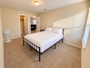 Un dormitorio con cama, ventilador y puerta que da a otra habitación.