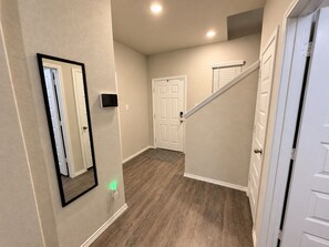 Un pasillo con piso de madera, una puerta blanca y una escalera con barandilla blanca.