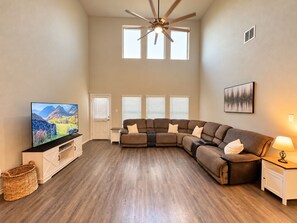 Una sala de estar con sofá modular, televisor, ventilador de techo y chimenea.