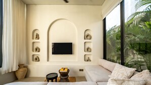 A modern bedroom with a large bed, a TV mounted on the wall, and a view of greenery outside. - Casanna Umalas (Kerobokan)