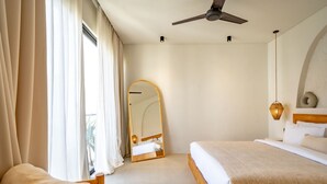 A hotel room with a bed, a chair, a ceiling fan, a large mirror, and a window with curtains. - Casanna Umalas (Kerobokan)