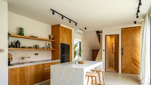 A modern kitchen with wooden cabinets, a marble countertop, and a central island with bar stools. - Casanna Umalas (Kerobokan)