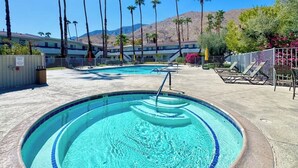En swimmingpool med krystalklart, blå vand, omgivet af palmer og et bjergrigt landskab.
