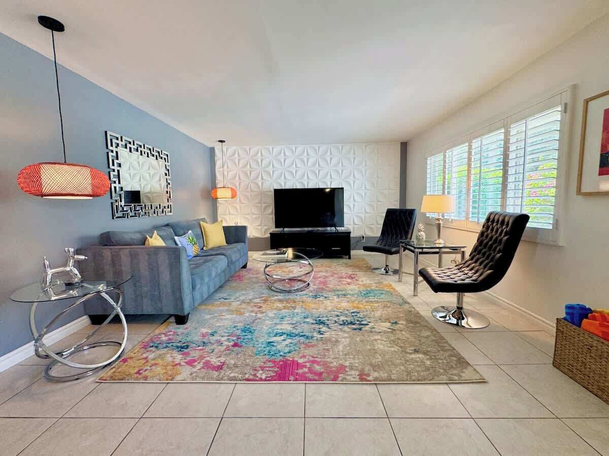 Un salon avec un canapé, un téléviseur, un tapis à motifs, un fauteuil et une petite table.