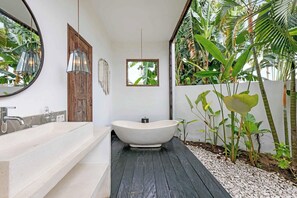 Un baño moderno con una bañera independiente, un espejo grande y una ventana pequeña.