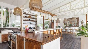 A spacious kitchen with a central island, wooden cabinets, and hanging pendant lights. - Umalas 5BR Bohemian Escape • Rice Fields + Yoga & Spa w/ 12min To Beach (Badung)