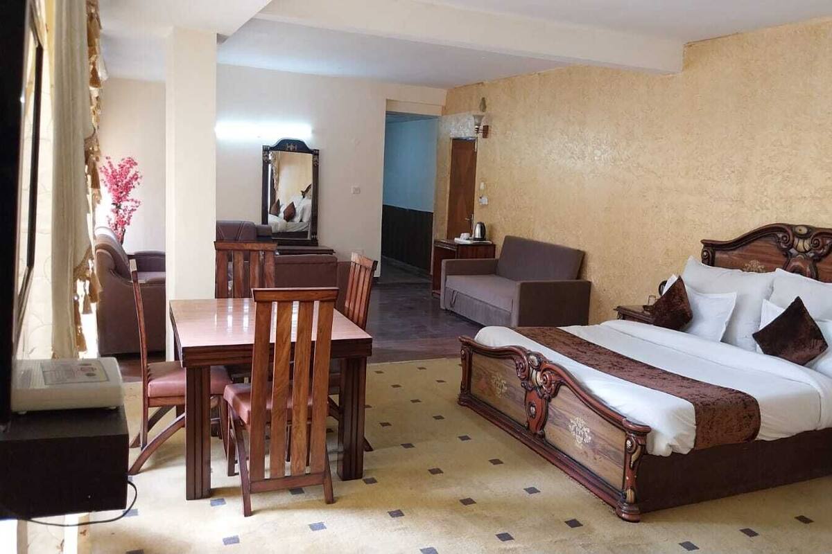 A hotel room with a wooden bed, a desk with a chair, a sofa, and a mirror.