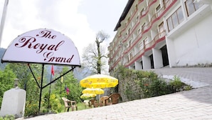 Placa do hotel 'The Royal Grand', com área de estar ao ar livre e um edifício ao fundo.