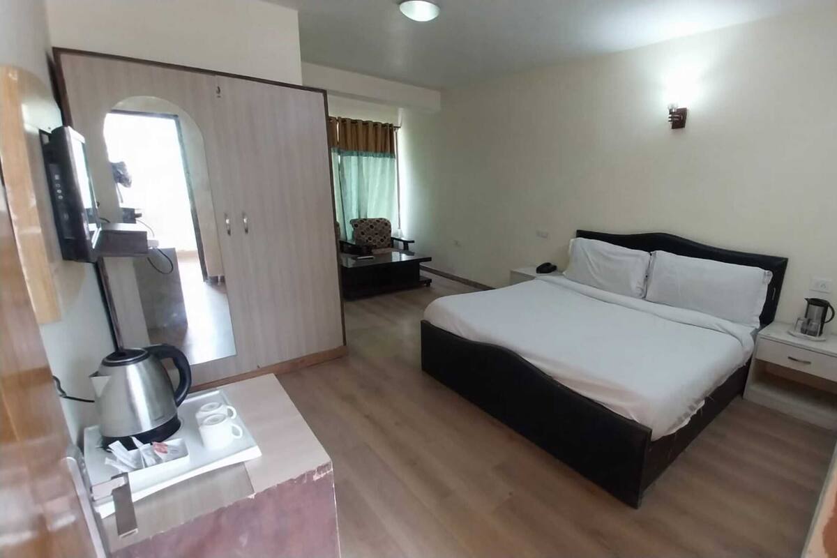 A hotel room with a bed, a desk with a kettle, a wardrobe, and a small table with a lamp.
