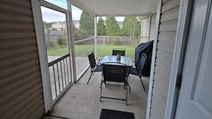 Un patio techado con mesa y sillas, vista al jardín trasero y cerca de madera.