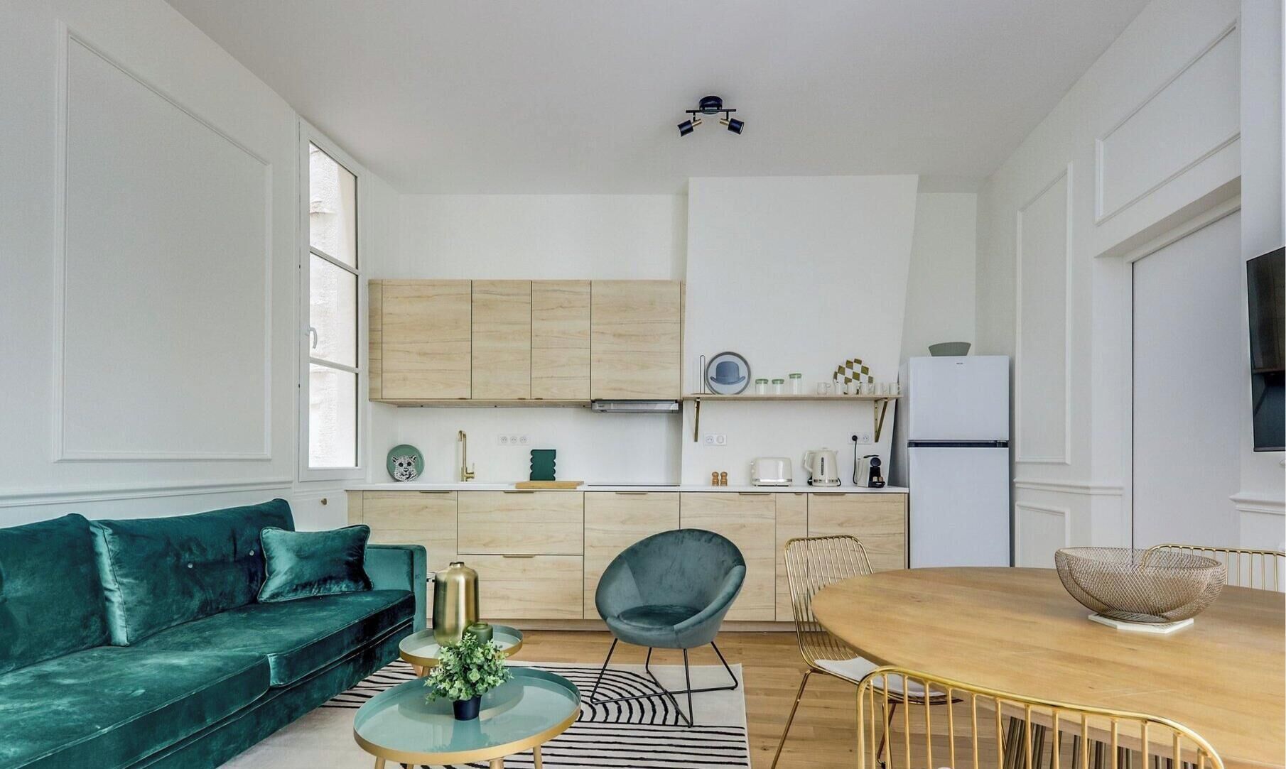 Eine moderne Küche mit Holdekor, ein Essbereich mit rundem Tisch und Stühlen sowie ein grünes Sofa.