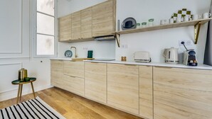 Eine moderne Küche mit hellen Holzschränken, einer weißen Arbeitsplatte und verschiedenen Geräten, darunter ein Wasserkocher, ein Toaster und eine Kaffeemaschine.