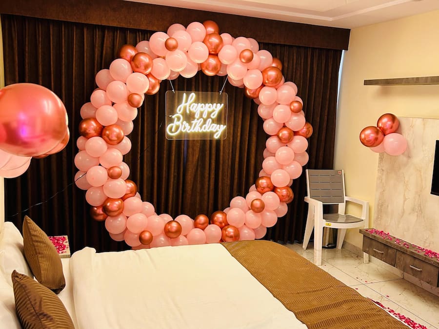 Una habitación de hotel con una cama, una silla, un escritorio y un letrero de neón que dice 'Happy Birthday'.