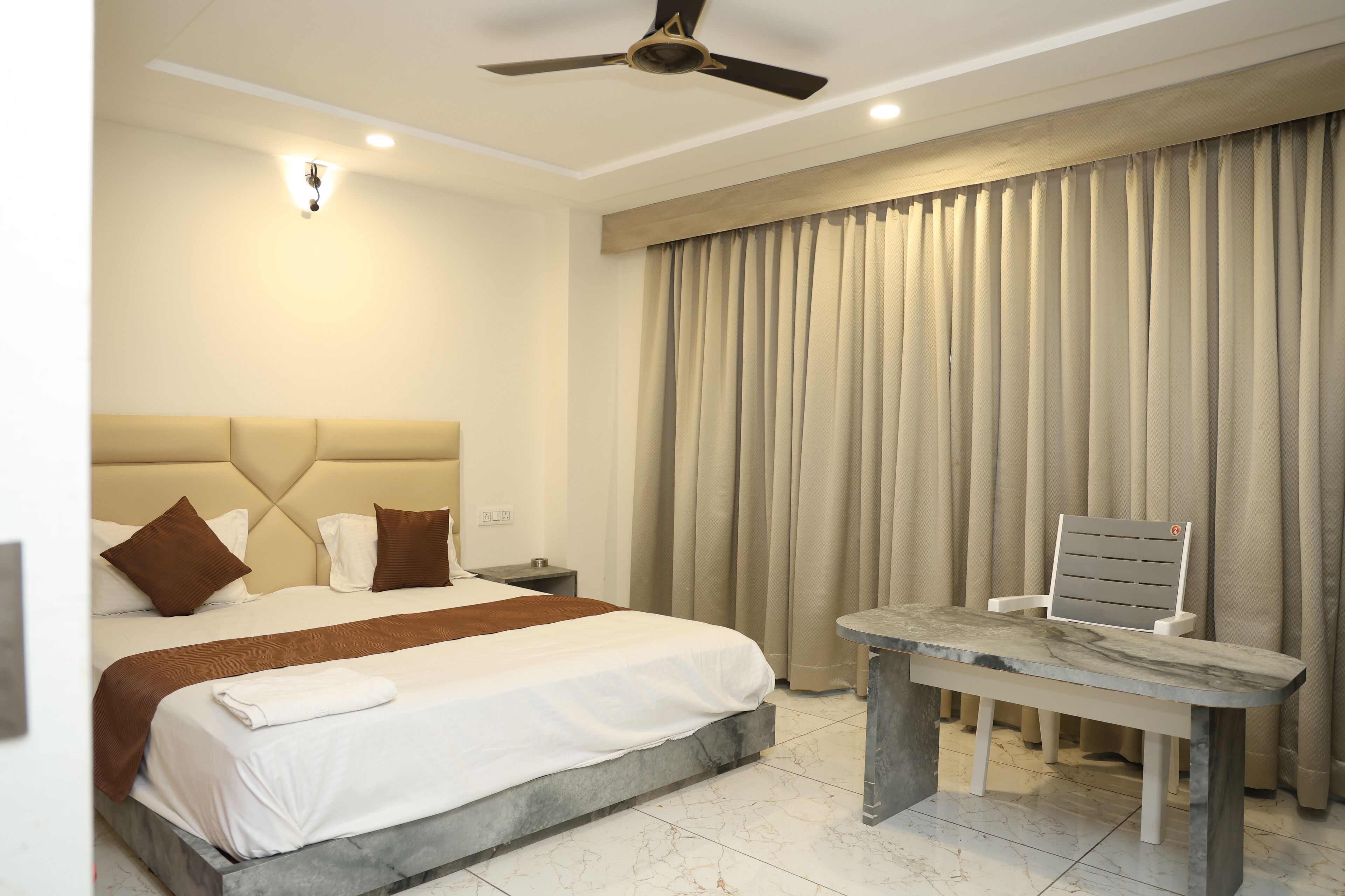 A hotel room with a bed, a desk, a chair, and a ceiling fan.