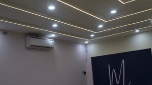 A modern interior with recessed ceiling lighting, a large abstract wall art piece, and green upholstered seating. - HOTEL MAGNET - INDORE (Indore)