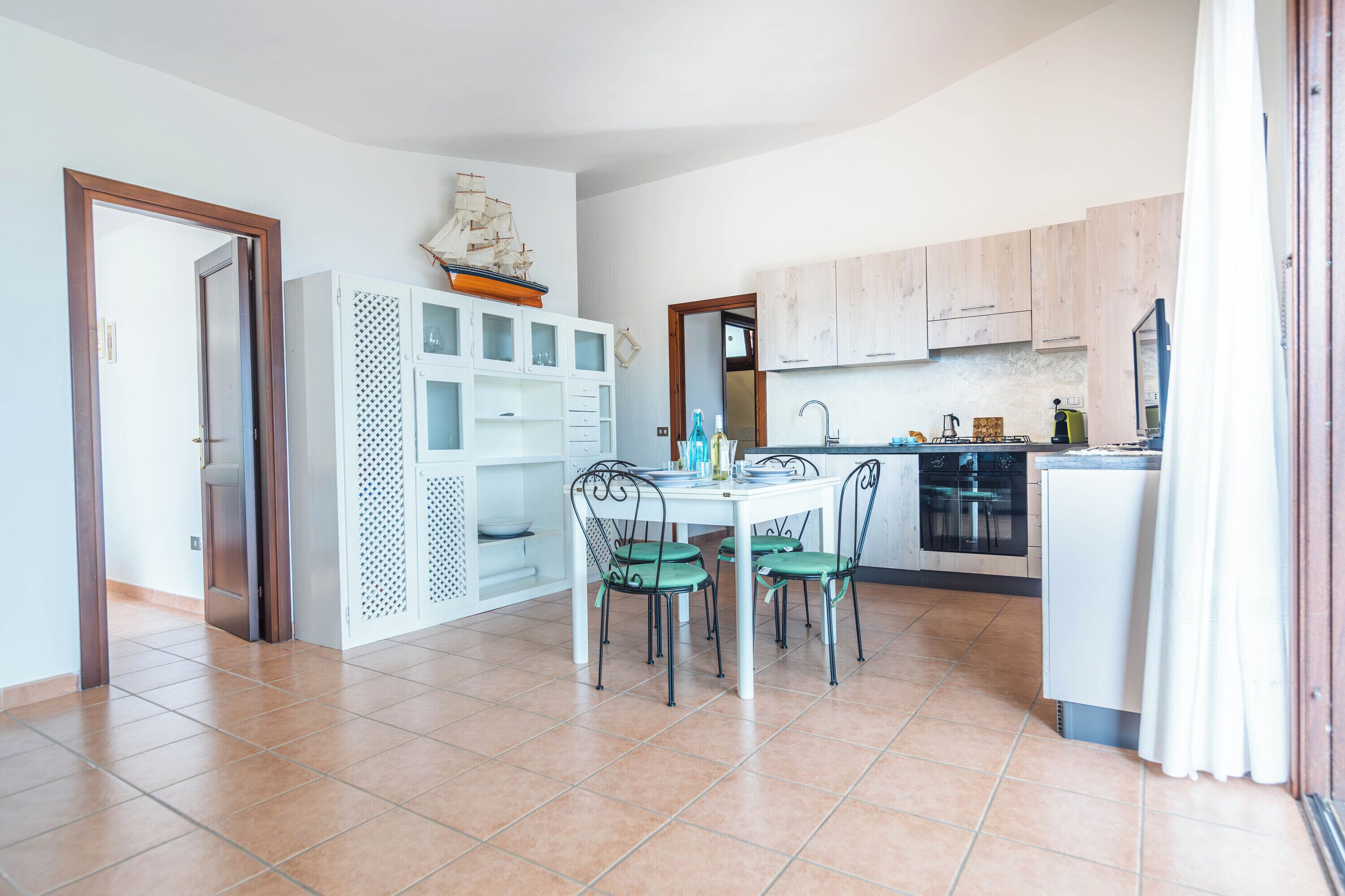Una cocina moderna con armarios blancos, una mesa de comedor con cuatro sillas y un modelo de barco en la pared.