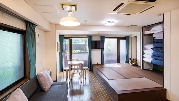 Ein Zimmer mit einer Couch, Tatami-Matten, einem kleinen Tisch und einem Fernseher.