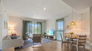 A modern living room with a sofa, a dining table, chairs, a TV, and a large window with curtains. - Bright Hollywood Two Bedroom with Free Parking (Hollywood)