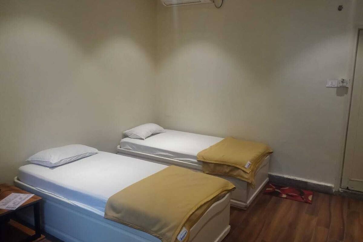 Ein Zimmer mit zwei Einzelbetten, jeweils mit Kissen und Decke. Es gibt einen kleinen Tisch mit einem Stuhl und eine Wand-Klimaanlage.