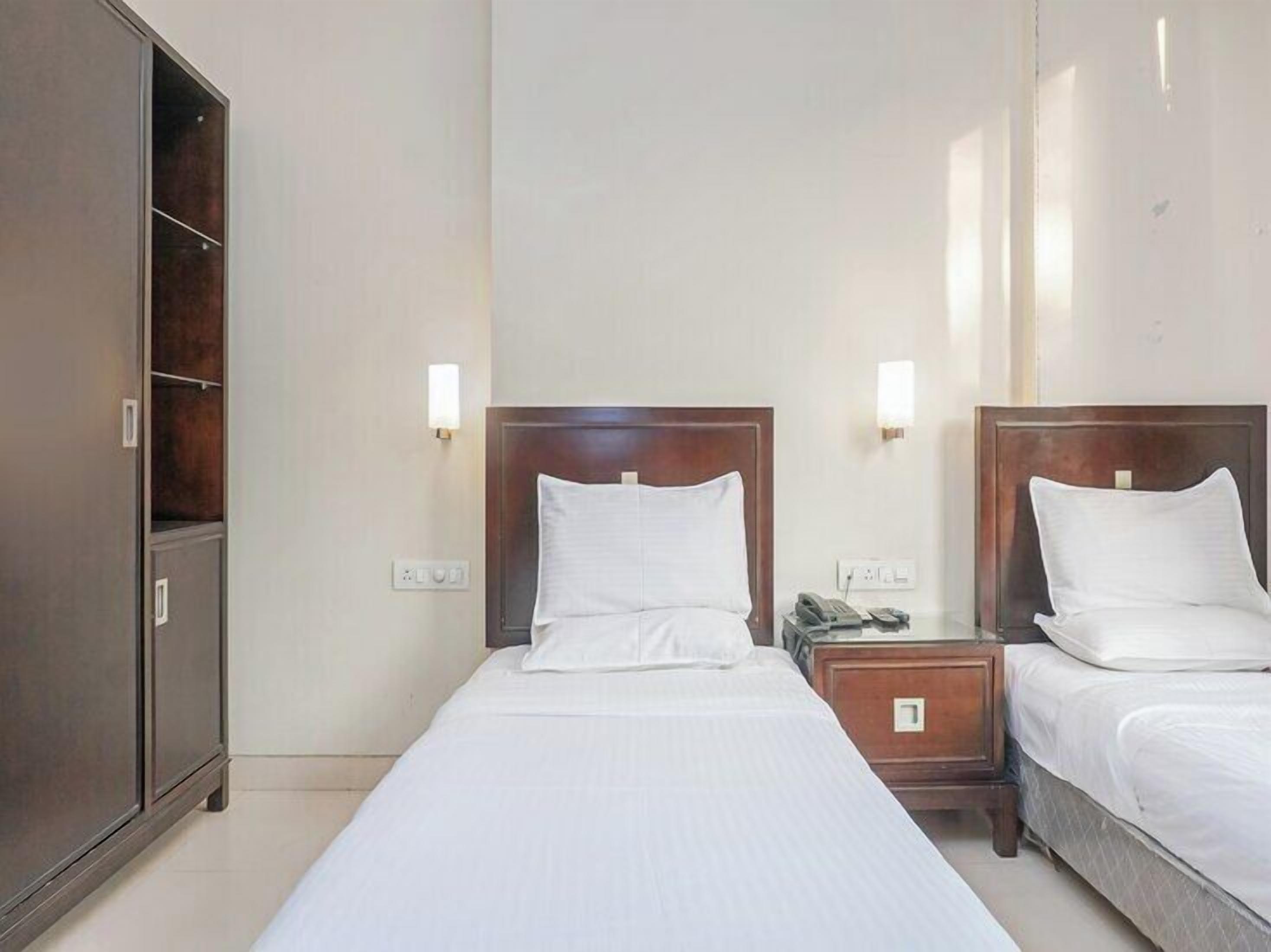 A hotel room with two single beds, a wardrobe, bedside lamps, and a telephone on the nightstand.