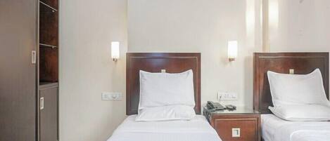 Una habitación de hotel con dos camas individuales, un armario, lámparas de noche y un teléfono en la mesita de noche.