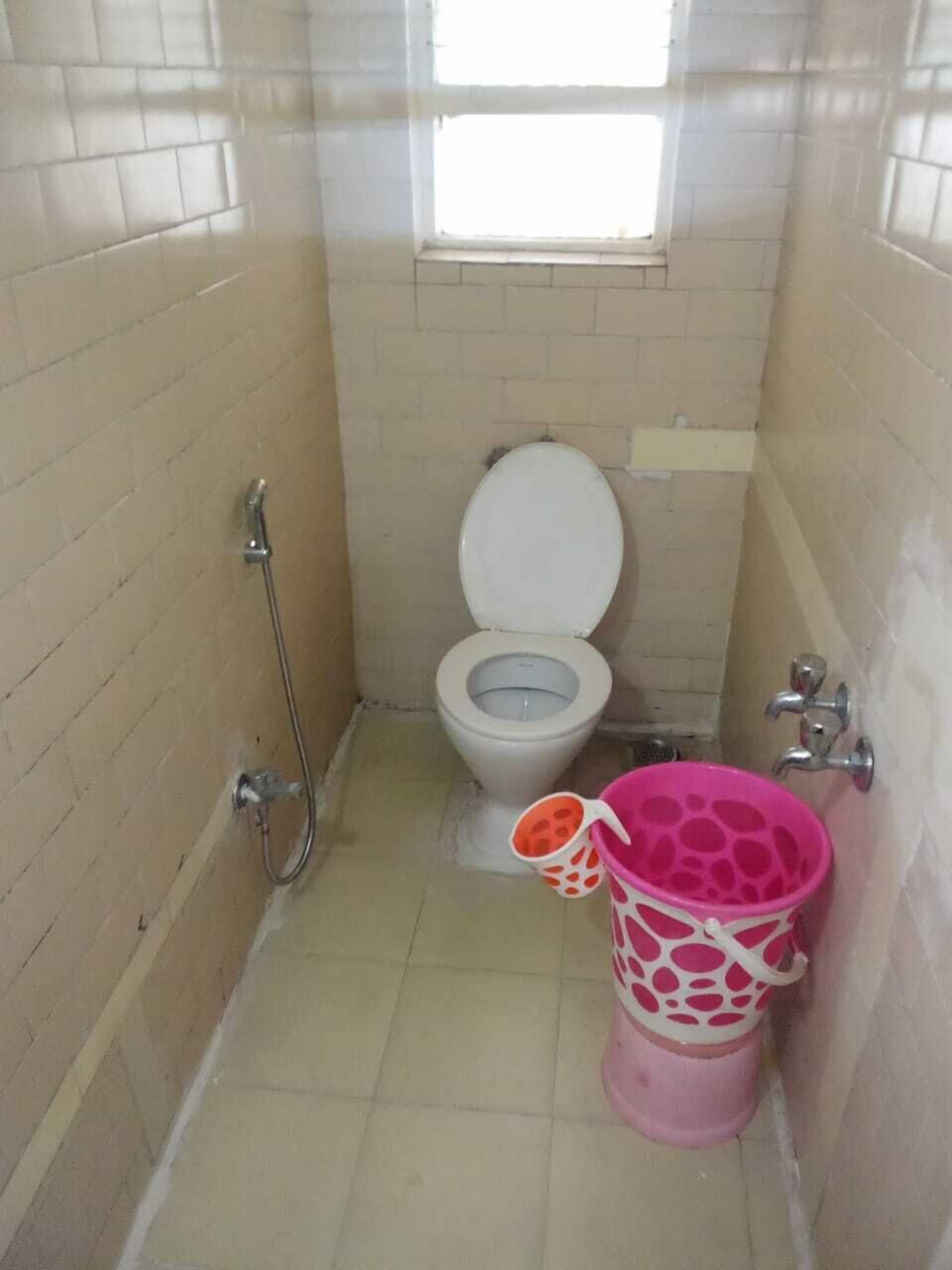 A small, tiled bathroom with a toilet, a shower, and a pink bucket.