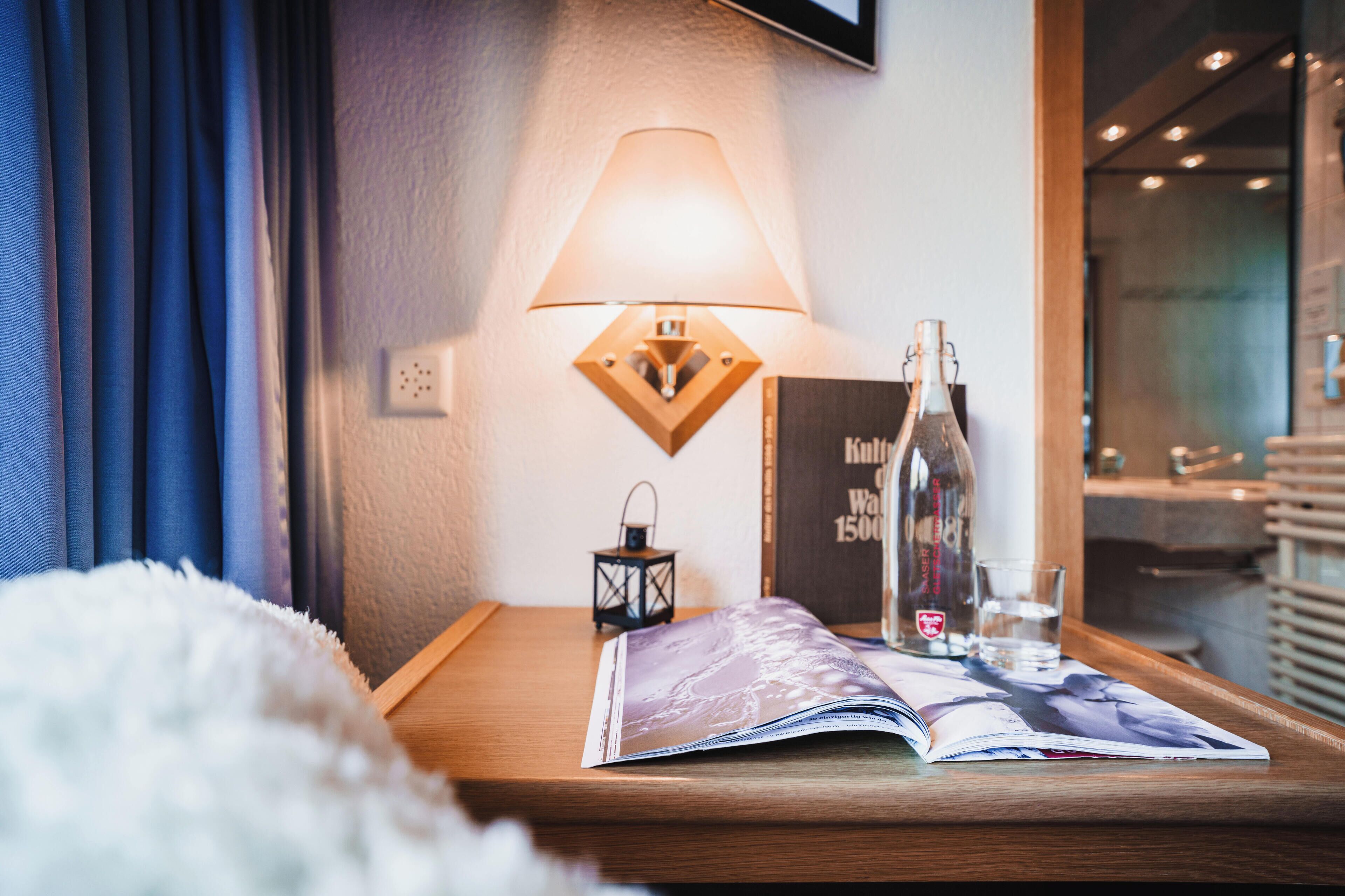 A neatly arranged bedside table with a lamp, a bottle, a glass of water, and a magazine.