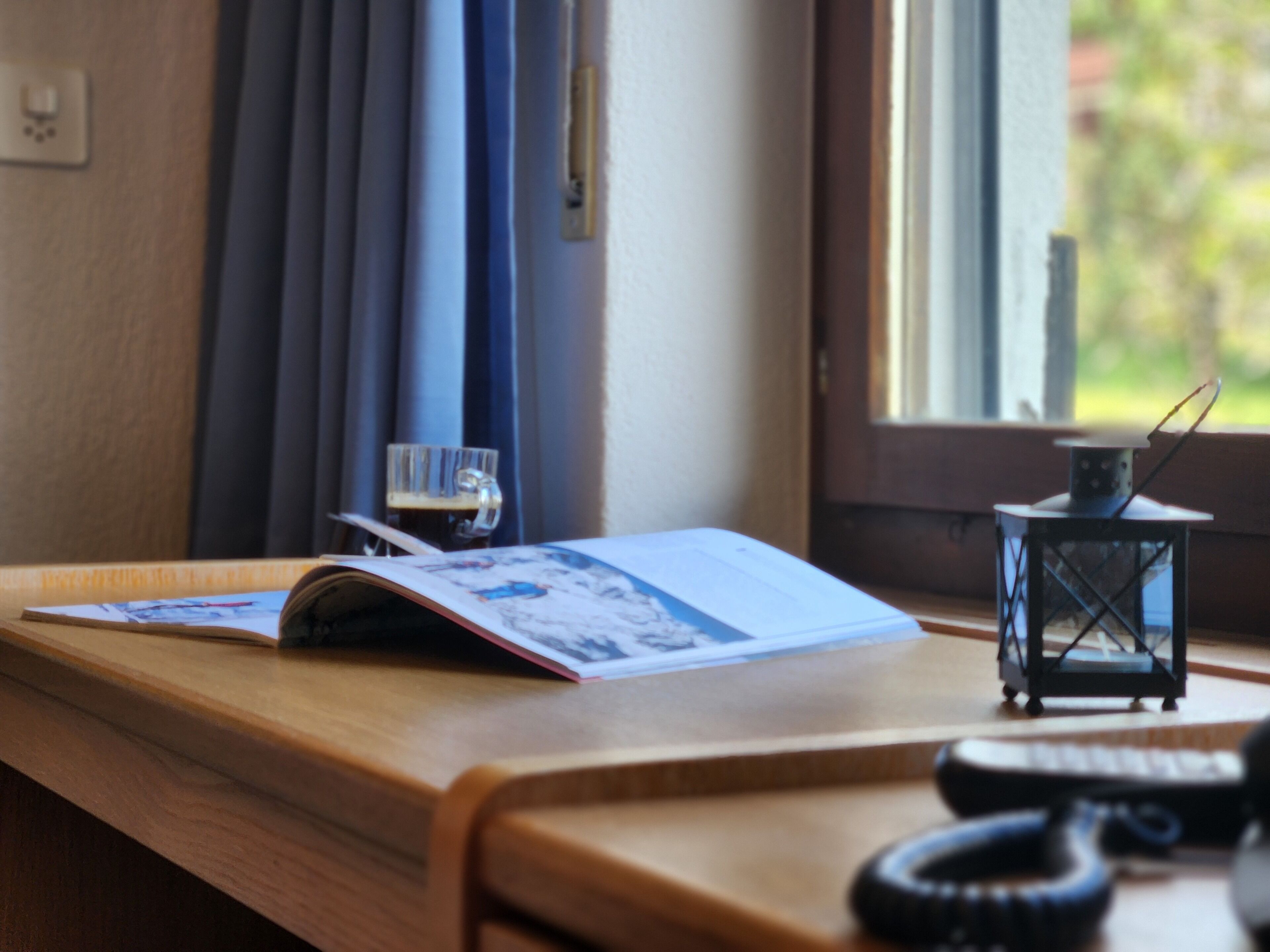 A wooden desk with a book, a glass of beer, and a lantern.