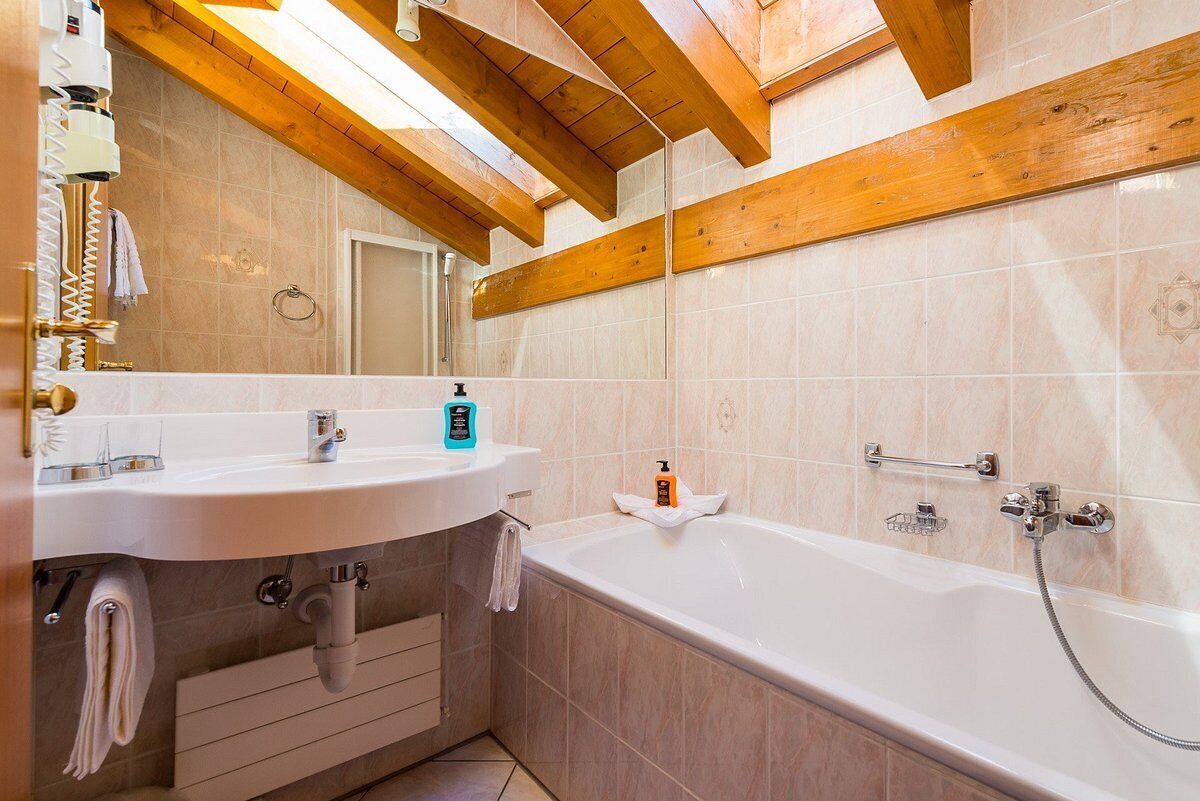 A modern bathroom with a wooden ceiling, a white sink, a bathtub, and a large mirror.