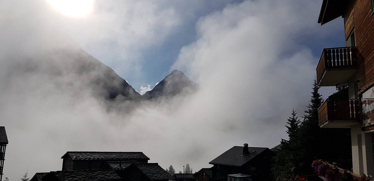 Una montaña con nubes que la cubren parcialmente, rodeada de edificios de arquitectura tradicional.