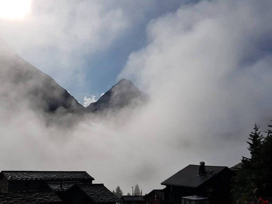 Una montaña con nubes que la cubren parcialmente, rodeada de edificios de arquitectura tradicional.