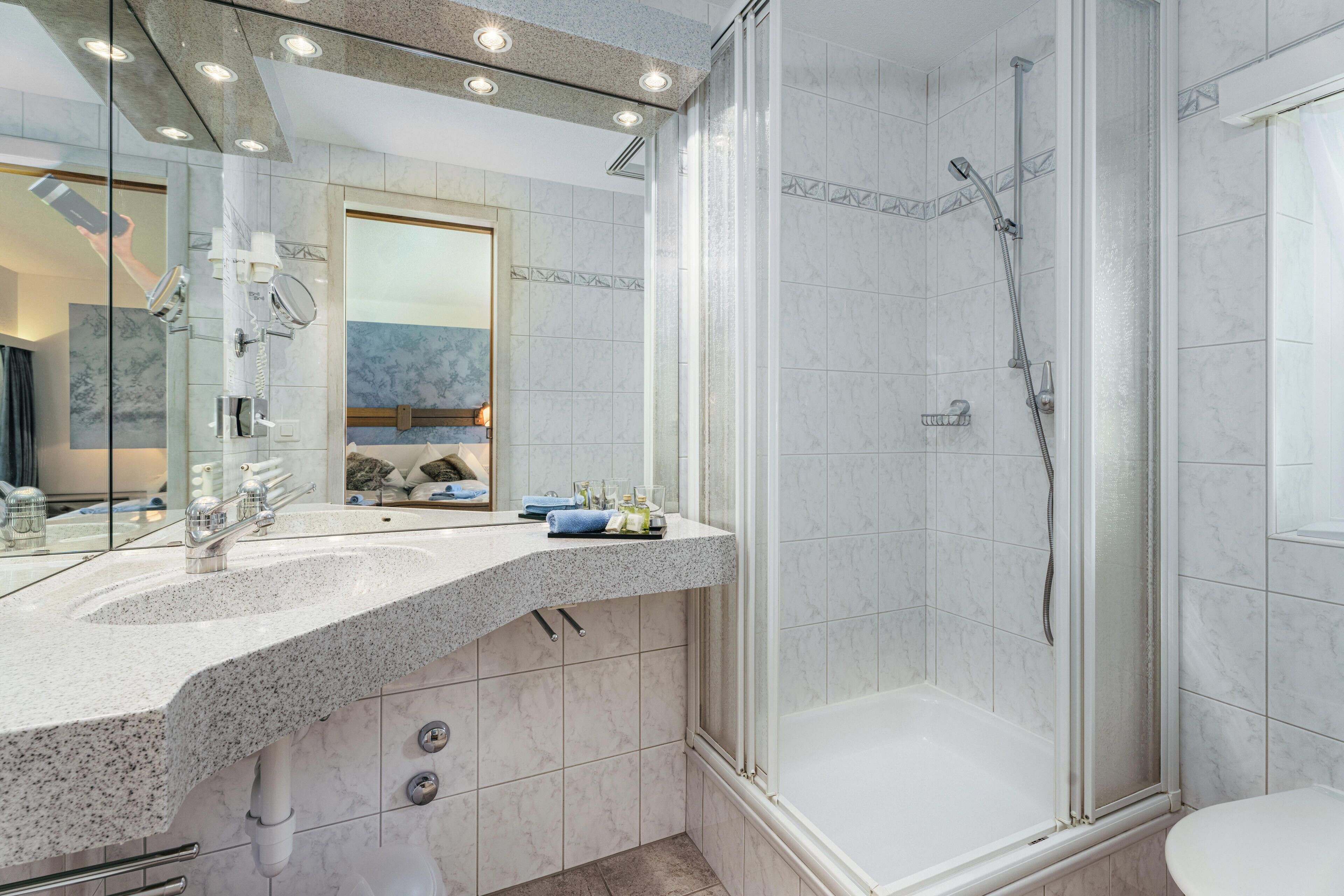 Un baño moderno con encimera de granito, ducha con mampara de vidrio y un espejo grande.