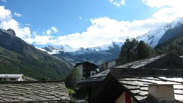A mountain village with traditional stone-roofed buildings and a view of snow-capped peaks in the background.