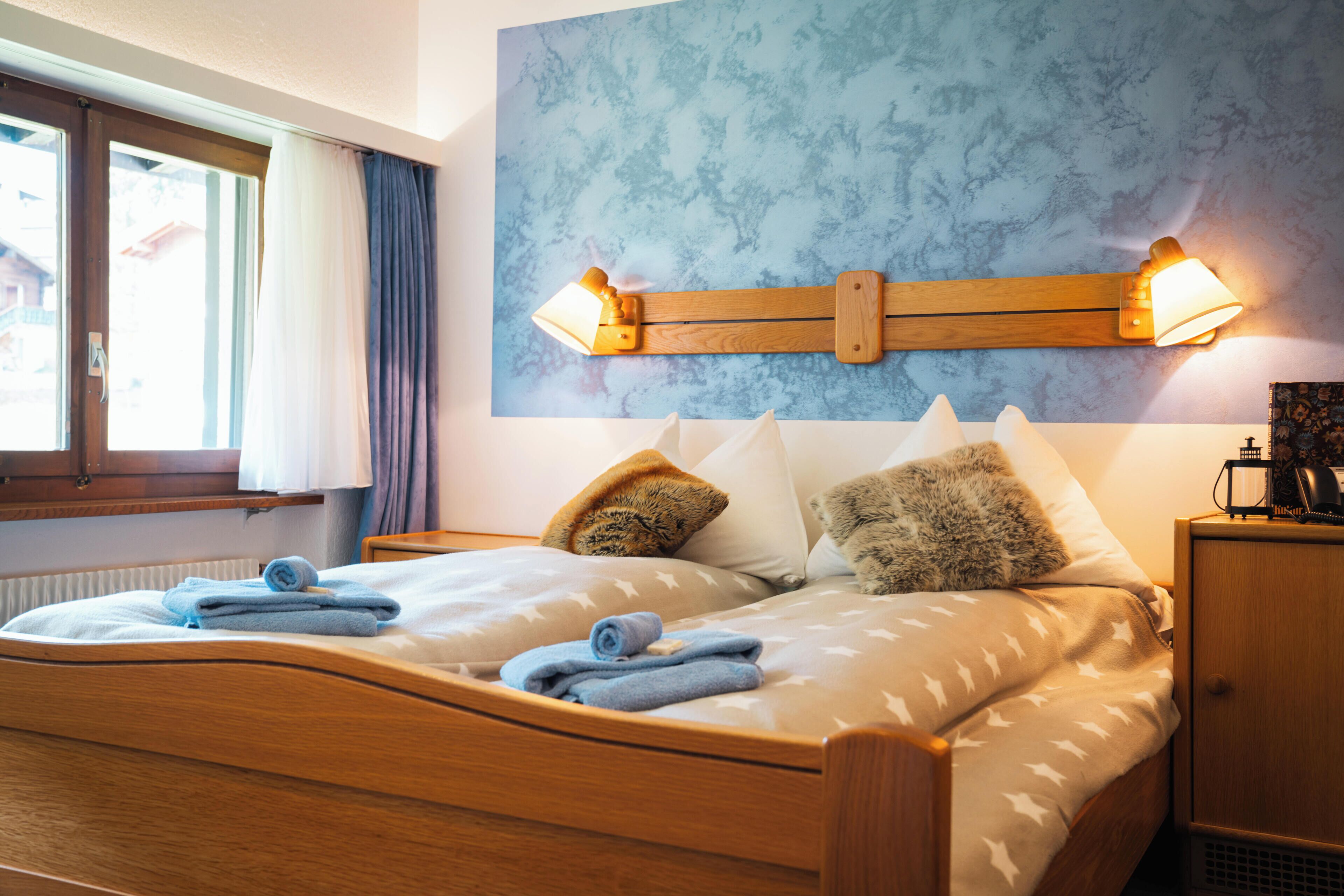 Un dormitorio con una cama de madera, dos lámparas fijadas a la pared y una ventana con cortinas.