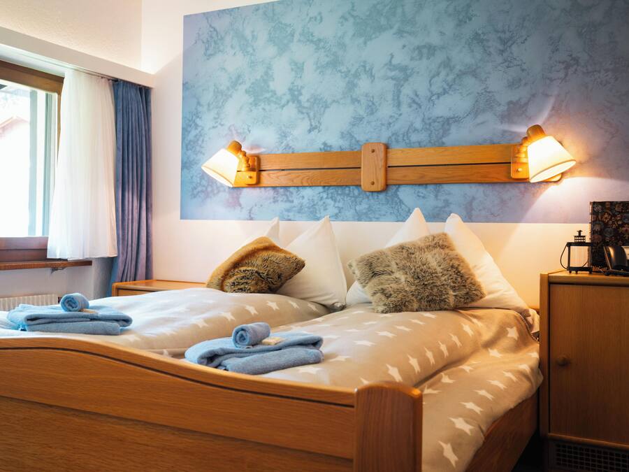 Un dormitorio con una cama de madera, dos lámparas fijadas a la pared y una ventana con cortinas.